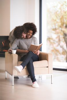 Young beautiful multiethnic couple hugging in front of fireplace at home when reading a book at autumn day