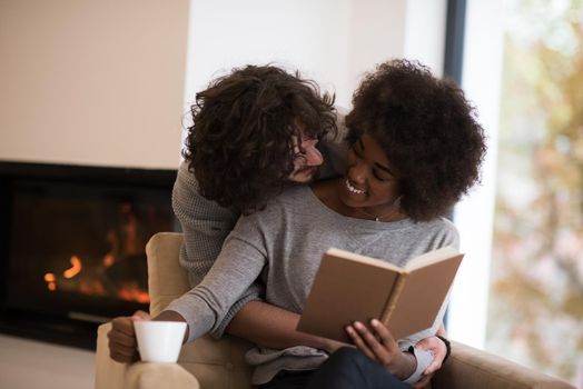 Young beautiful multiethnic couple hugging in front of fireplace at home when reading a book at autumn day