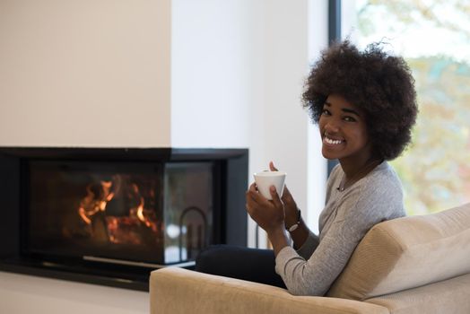 Happy joyful african american woman drinking cup of coffee relaxing at fireplace. Young black girl with hot beverage heating warming up. autumn at home.