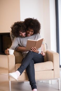 Young beautiful multiethnic couple hugging in front of fireplace at home when reading a book at autumn day