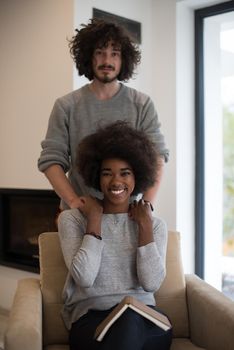 Young beautiful multiethnic couple hugging in front of fireplace at home when reading a book at autumn day