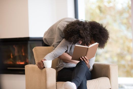 Young beautiful multiethnic couple hugging in front of fireplace at home when reading a book at autumn day