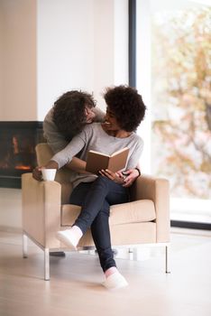 Young beautiful multiethnic couple hugging in front of fireplace at home when reading a book at autumn day