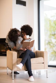 Young beautiful multiethnic couple hugging in front of fireplace at home when reading a book at autumn day