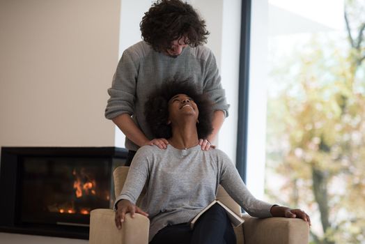 Young beautiful multiethnic couple hugging in front of fireplace at home when reading a book at autumn day