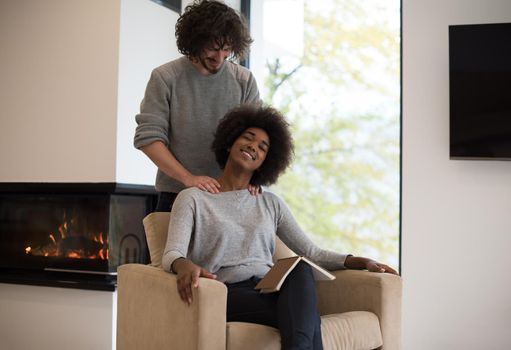 Young beautiful multiethnic couple hugging in front of fireplace at home when reading a book at autumn day