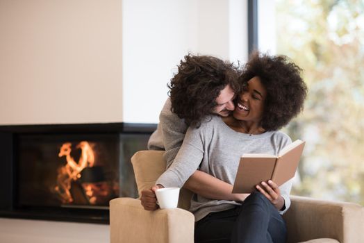 Young beautiful multiethnic couple hugging in front of fireplace at home when reading a book at autumn day