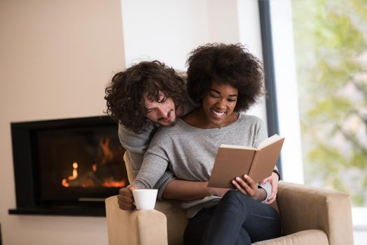 Young beautiful multiethnic couple hugging in front of fireplace at home when reading a book at autumn day