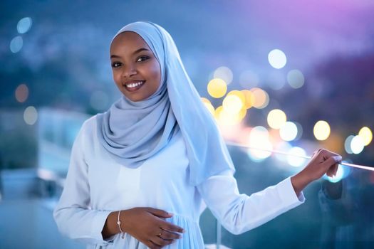 African  Muslim woman in night  at balcony  smiling at camera with city bokeh lights in background