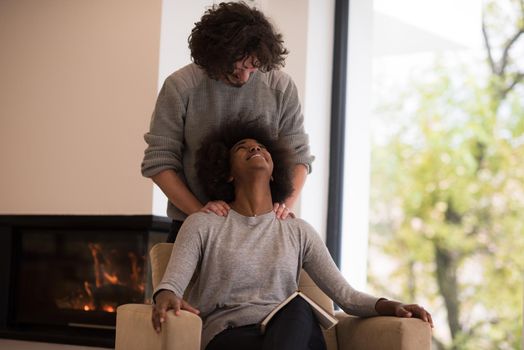 Young beautiful multiethnic couple hugging in front of fireplace at home when reading a book at autumn day