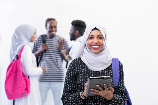 young african modern muslim female student using tablet computer with group of friends in background  wearing traditional Islamic hijab clothes
