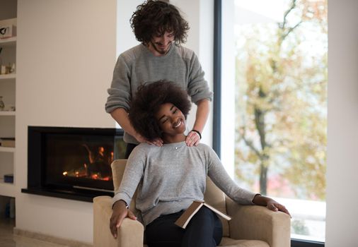 Young beautiful multiethnic couple hugging in front of fireplace at home when reading a book at autumn day