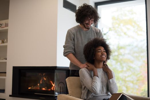 Young beautiful multiethnic couple hugging in front of fireplace at home when reading a book at autumn day