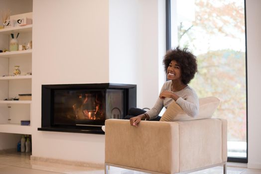 Young beautiful african american woman relaxing on chair in front of fireplace at autumn day