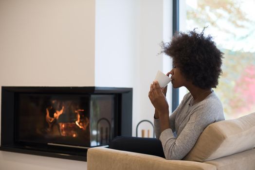 Happy joyful african american woman drinking cup of coffee relaxing at fireplace. Young black girl with hot beverage heating warming up. autumn at home.