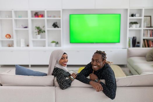 African Couple Sitting On Sofa Watching TV Together Chroma Green Screen Woman Wearing Islamic Hijab Clothes