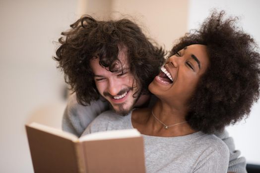 Young beautiful multiethnic couple hugging in front of fireplace at home when reading a book at autumn day