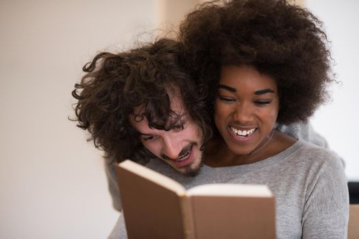 Young beautiful multiethnic couple hugging in front of fireplace at home when reading a book at autumn day