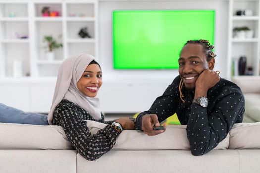 African Couple Sitting On Sofa Watching TV Together Chroma Green Screen Woman Wearing Islamic Hijab Clothes