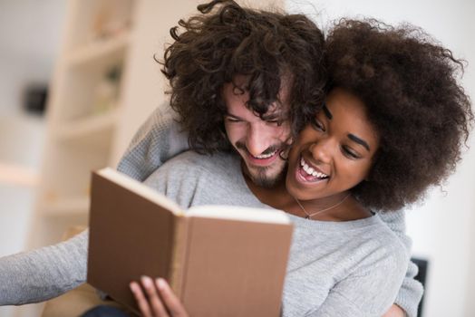 Young beautiful multiethnic couple hugging in front of fireplace at home when reading a book at autumn day