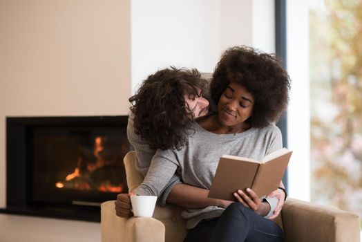 Young beautiful multiethnic couple hugging in front of fireplace at home when reading a book at autumn day