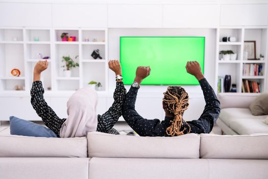 African Couple Sitting On Sofa Watching TV Together Chroma Green Screen Woman Wearing Islamic Hijab Clothes