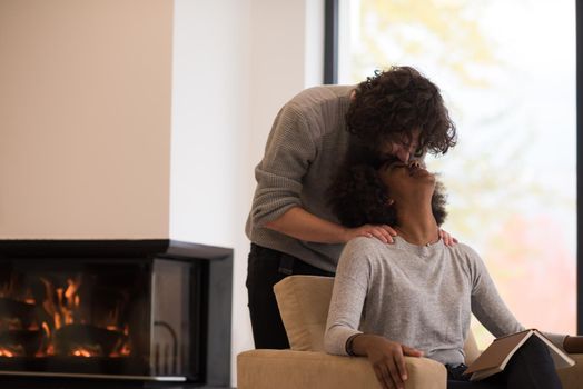 Young beautiful multiethnic couple hugging in front of fireplace at home when reading a book at autumn day