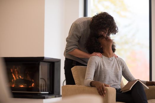 Young beautiful multiethnic couple hugging in front of fireplace at home when reading a book at autumn day