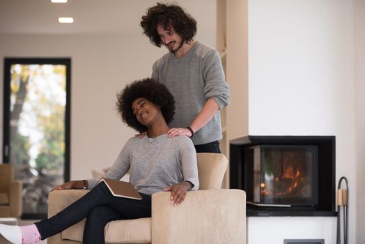 Young beautiful multiethnic couple hugging in front of fireplace at home when reading a book at autumn day