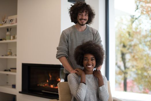 Young beautiful multiethnic couple hugging in front of fireplace at home when reading a book at autumn day