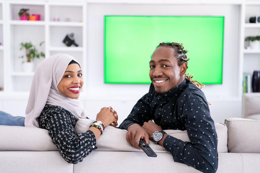 African Couple Sitting On Sofa Watching TV Together Chroma Green Screen Woman Wearing Islamic Hijab Clothes