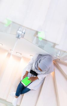 young african modern muslim woman using tablet computer while sitting on the stairs at home  wearing hijab clothes  top view