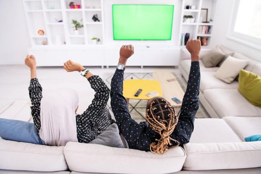 African Couple Sitting On Sofa Watching TV Together Chroma Green Screen Woman Wearing Islamic Hijab Clothes