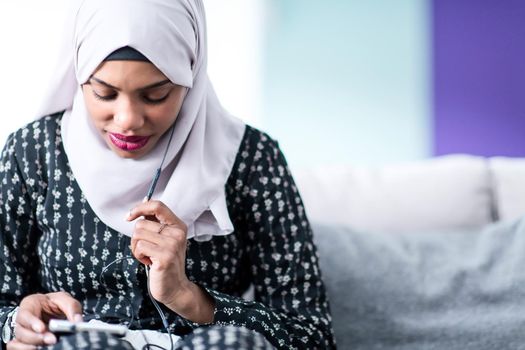african woman using smartphone while sitting on sofa at home  wearing hijab clothes