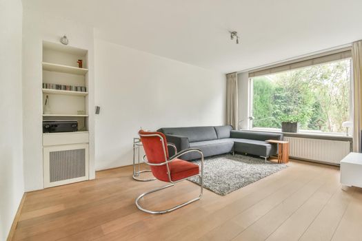 Stylish living room with corner gray sofa and bright red armchair
