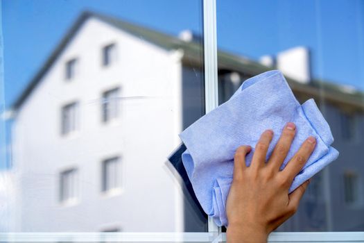 Woman cleans her house, female hand holds a rag and with detergent washes the window to perfect condition, a modern building is reflected in the window close up view with creative concept.