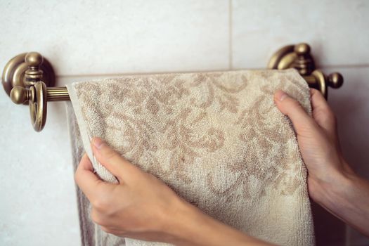 Female hands hang a fresh clean towel on a towel holder made in vintage style in the bathroom.