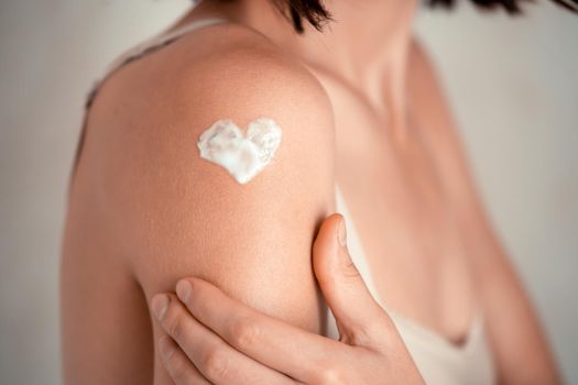 A young girl applies a moisturizer to her skin, a woman gently cares for her body, depicts a heart with a cream, taking care of herself, beauty and health.