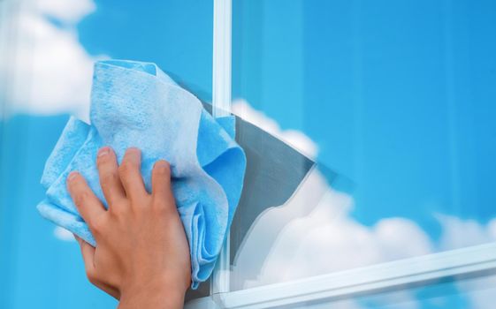 A woman's hand holds a cloth to wipe surfaces and washes the windows of her house to perfect cleanliness and freshness, a creative concept with a close-up of a reflecting sky.