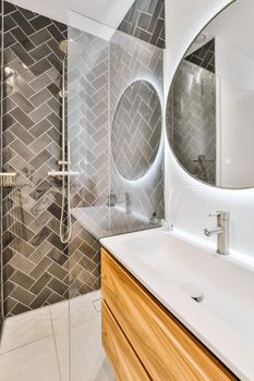 Stunning bathroom with large round illuminated mirror and sink with wooden cabinet