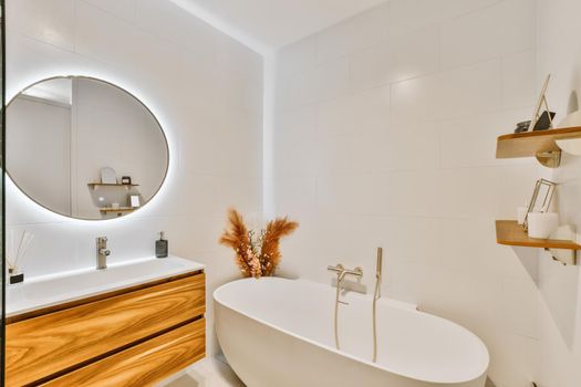 Stunning bathroom with large round illuminated mirror and sink with wooden cabinet