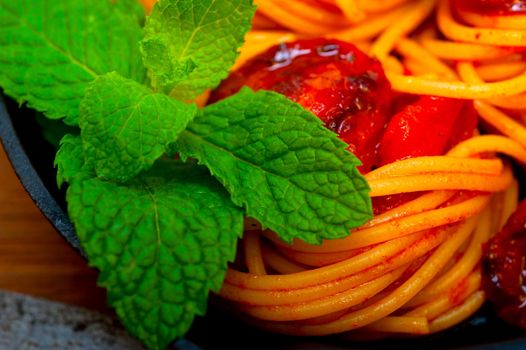 italian spaghetti pasta and tomato with mint leaves on iron skillet over wood board 