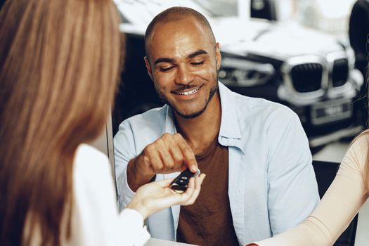 Salesperson giving key to buyer in a car salon close up