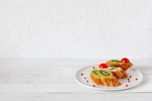 three homemade bright mini sandwichs with cream cheese and vegetables, on a white plate on wooden background, side view, copy space