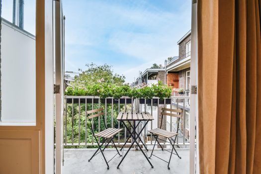Open door with curtains opening onto a balcony with wooden table and chairs