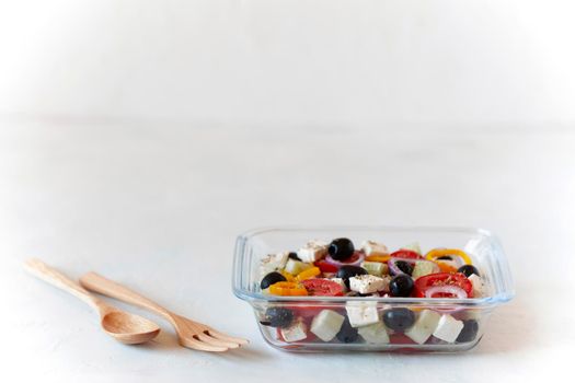 Greek salad in a glass container with a wooden cutlery, copy space, concept of eating at work