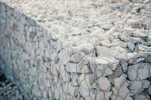 strengthening the slope with stones behind the wire. grey texture. construction. Granite stones behind a metal grate