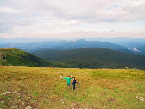 Aerial view of the Great Green Ridge. Guy and Girl Standing on a Big Hill against the Backdrop of a Huge Mountain Landscape.