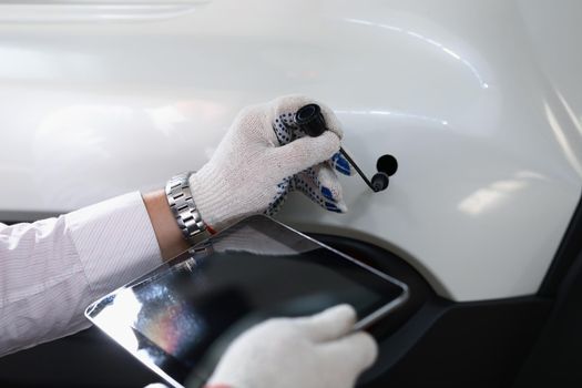 Close-up of male automechanic holding modern digital tablet and car tube in white gloves. Mechanic worker at service station. Automotive check, fix concept