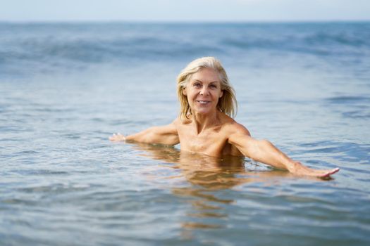 Older woman in good shape bathing in the sea. Elderly female enjoying her retirement at a seaside retreat.